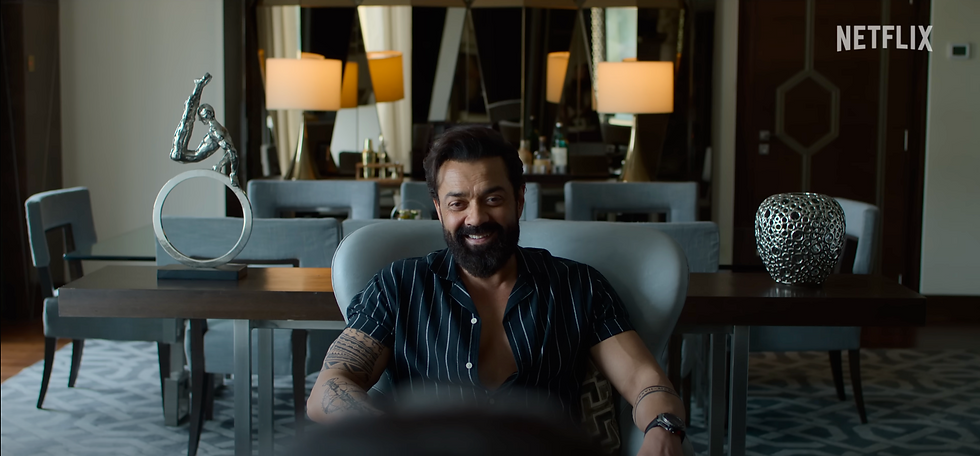 Bobby Deol in Ba**ds of Bollywood Netflix series, smiling while seated in a luxury apartment setting.