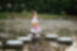 a girl twirls on a stepping stone at maymont for a senior portrait photographer in richmond and looks at the camera