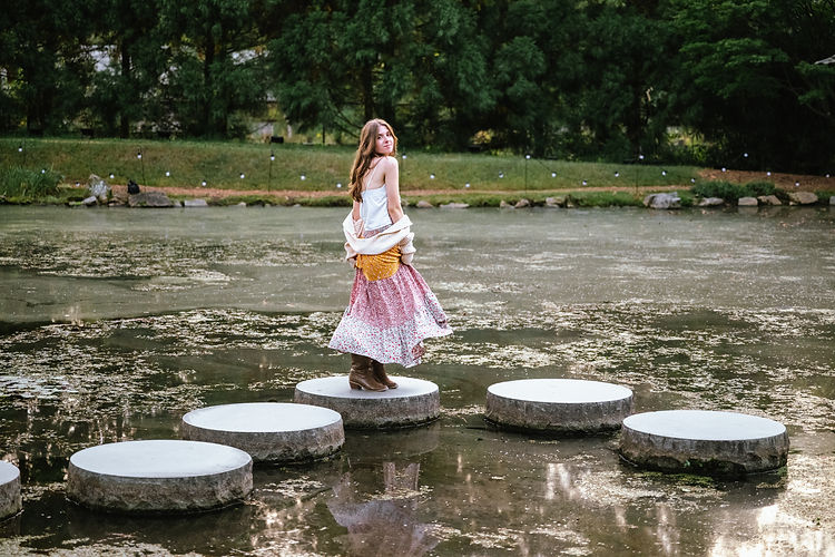 a girl twirls on a stepping stone at maymont for a senior portrait photographer in richmond and looks at the camera