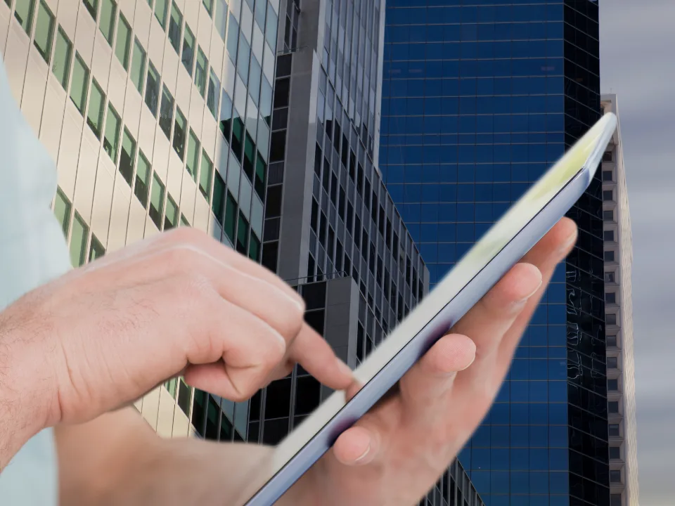Gestor consultando um tablet diante de edifícios corporativos espelhados