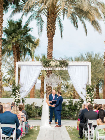 Bride and groom hold hands under white gazebo during ceremony