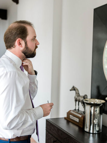 Groom ties his tie in front of a mirror