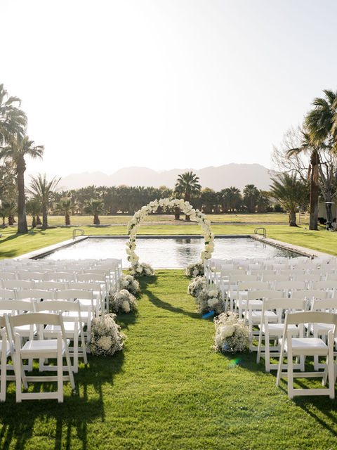 Wedding ceremony setup in front of pool. White chairs and white flowers.