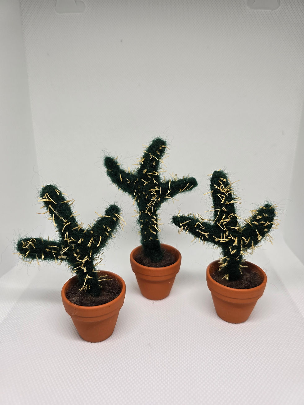 Three mini felted cactus in pots stand against a white background.