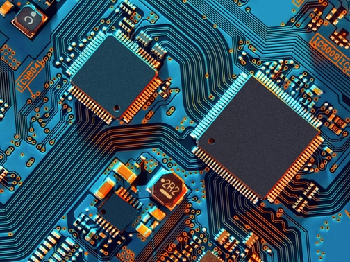Close-up of blue circuit board with two black microchips, orange traces, and labels like 2R2 and IC500.
