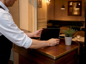 Host setting down dark tablet at restaurant podium