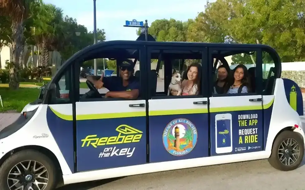 Une voiturette électrique ouverte de type navette "Freebee" avec des passagers à bord, portant des inscriptions publicitaires et le logo "Village of Key Biscayne