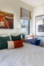 Bedroom with striped bedding, colorful pillows, and a desk by the window. A bull painting and "Learn" poster add charm. Cozy vibe.