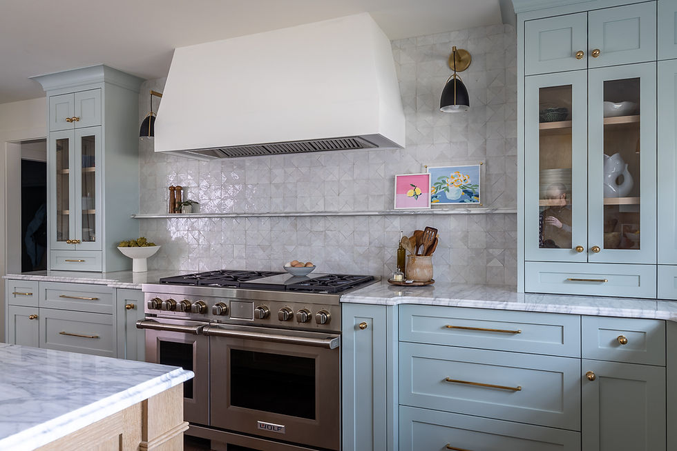 Modern kitchen with light blue cabinets, stainless steel stove, marble countertops, and patterned tile backsplash. Art pieces add color.