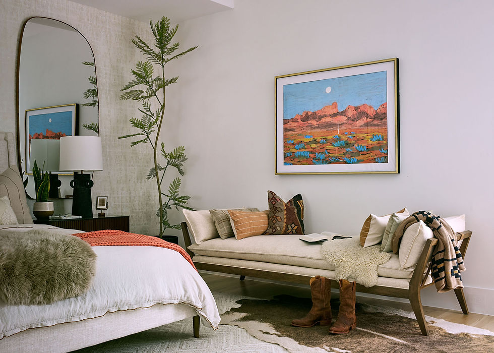 Cozy bedroom with a bed and daybed, decorated pillows, and boots. A landscape painting and tall plant adorn a serene, neutral space.