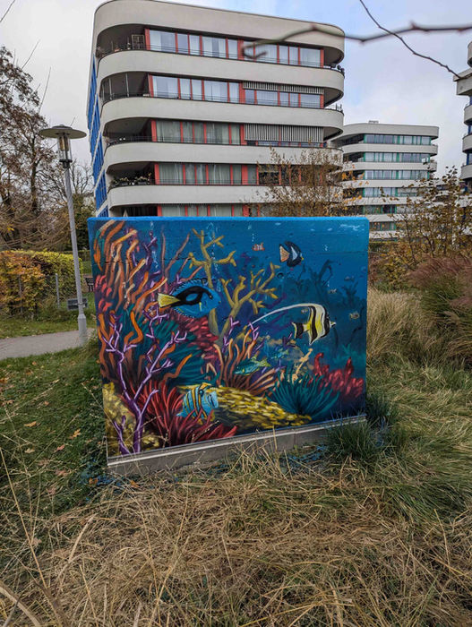 Unterwasser Wandmalerei mit Fischschwarm auf Lüftungsschacht, künstlerische Aufwertung einer Wohnsiedlung Zürich 2025