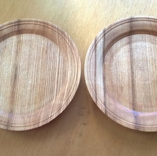 Two wooden plates displayed on a wooden table, with natural grain patterns clearly visible.