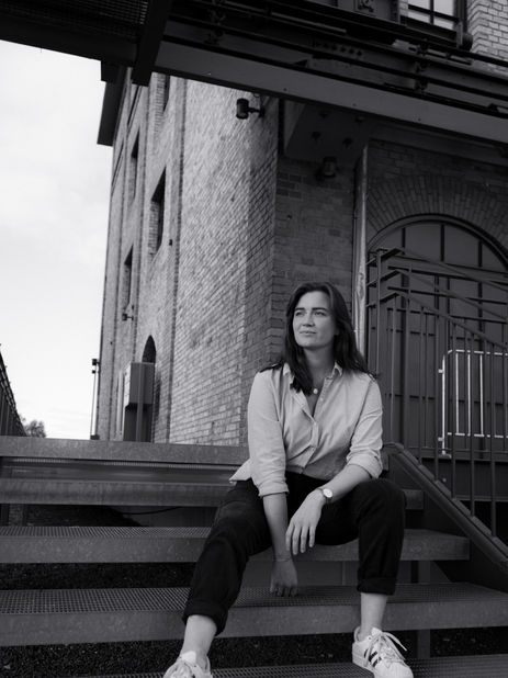 A woman sitting on stairs, behind her a brownstone house