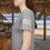Thumbnail: gray tee on a female model wearing a black tee shirt with a small American flag on the sleeve