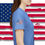 Thumbnail: A young lady wearing a light blue tee shirt with an American flag on the sleeve American flag Background