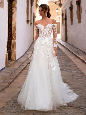 FISELLE from the Love collection frames the figure with an A-Line silhouette that feels poised and romantic. A sweetheart neckline and princess-boned bodice sculpt the upper body, while the Basque waist creates a beautifully defined shape before the skirt falls into graceful movement. Long sleeves add a refined, elongated line, and the chapel train lends a soft sense of ceremony as it trails behind. This bridal dress balances structure and romance with striking ease, leaving an impression that is both polished and quietly unforgettable.