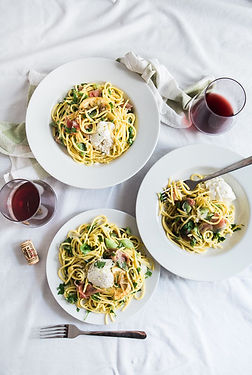 Three plates of pasta and red wine on a table with white tablecloth