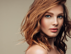 Jauna moteris su garbanotais rudais plaukais ir žydromis akimisdemonstruoja sveikus, blizgančius plaukus po grožio procedūrų