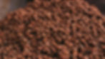 A close-up of a large pile of brown dried tigernuts with a blurred background, highlighting the texture and earthy color tones.