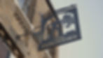 Black metal sign of a worker pouring molten metal, labeled "The Foundry," hangs on a brick building in Canterbury. Blue sky background.