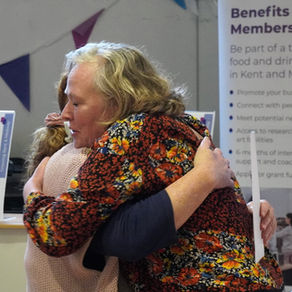Two women hugging in front of Growing Kent & Medway's display at Sunflower House.