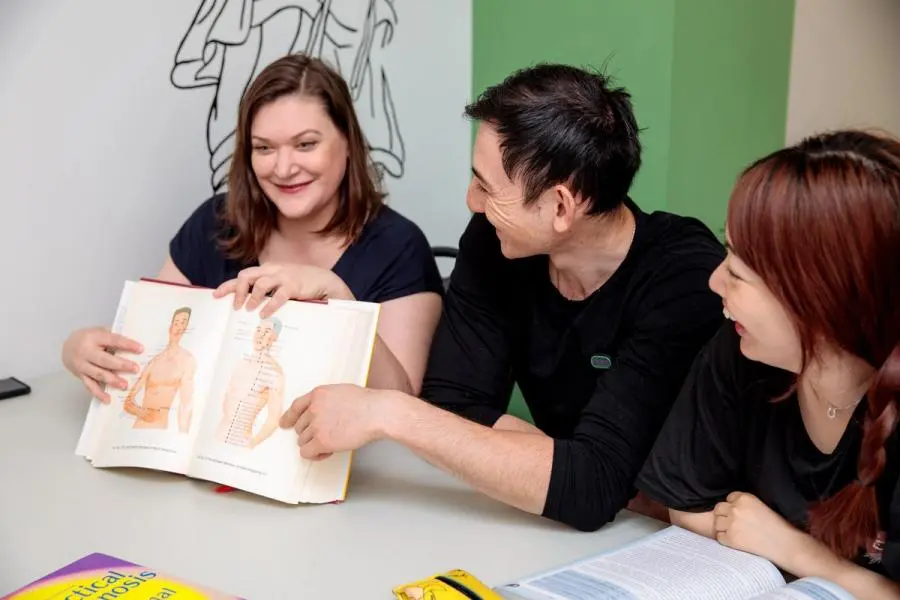 an acupuncture student group studying together and pointing at an image of an acupuncture diagram.