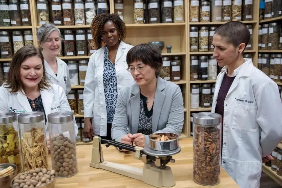 a group of students gathered around an instructor in a TCM apothecary, learning about herbs and TCM formulas.