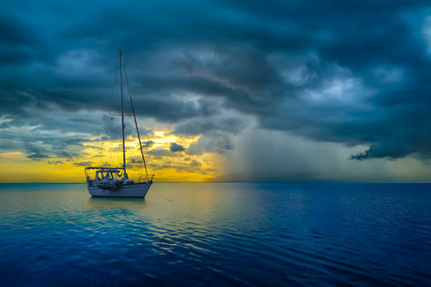 A sailboat anchored for the night with rain close by. 