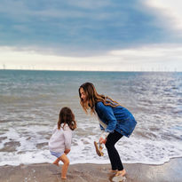Mia plays with her daughter on the beach, waves lapping at the shore,