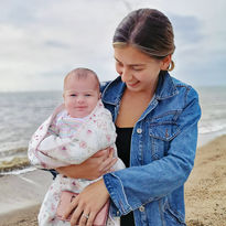 Mia, in a denim jacket, smiling at her baby daughter by the beach.