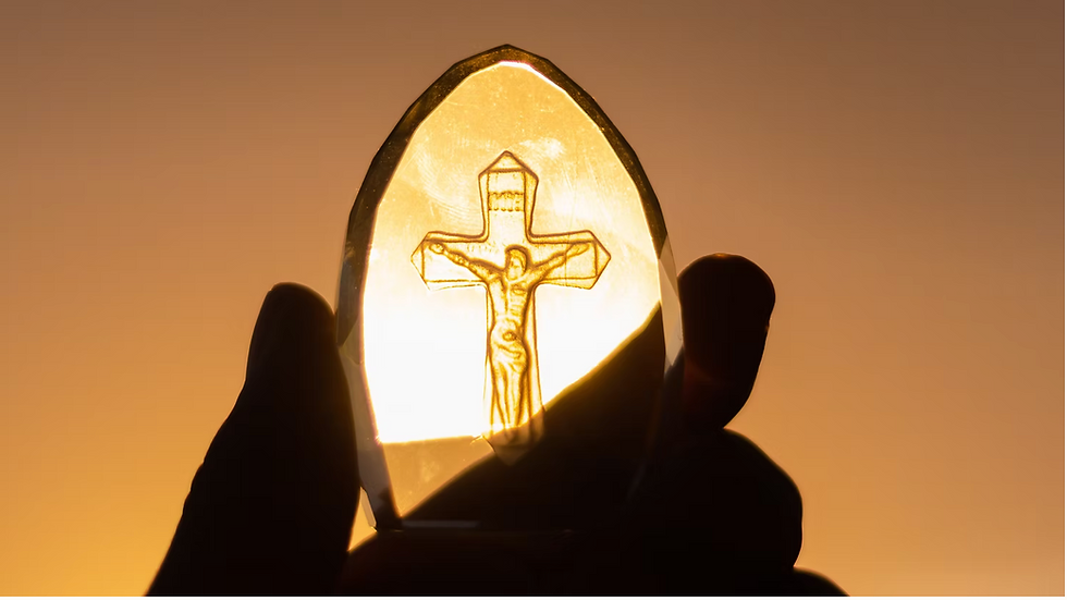 Hand holds a glowing crucifix-shaped glass pendant against a golden sunset sky.
