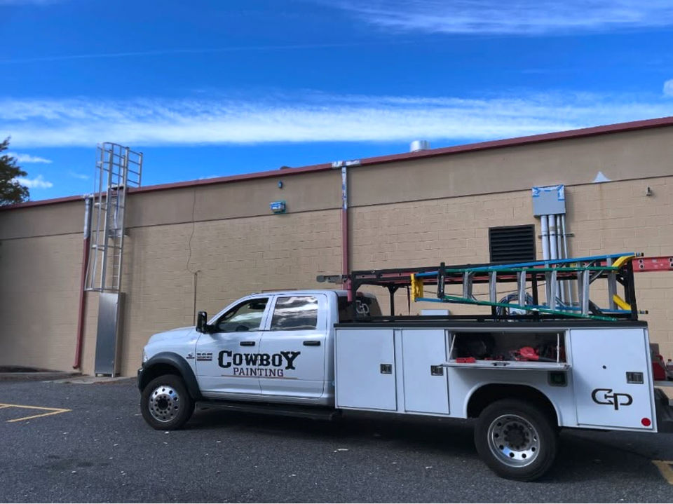 Cowboy Painting Co.'s 4-door RAM 5500 diesel truck parked in front of a commercial shopping center, ready for the next phase of a large exterior painting project