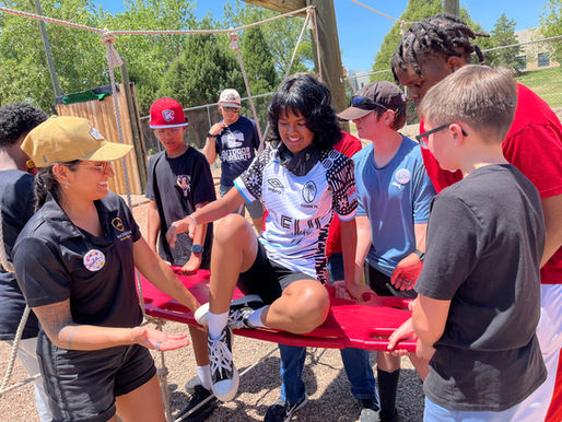 Students work together as a group to lift a girl on a plank at a ropes course