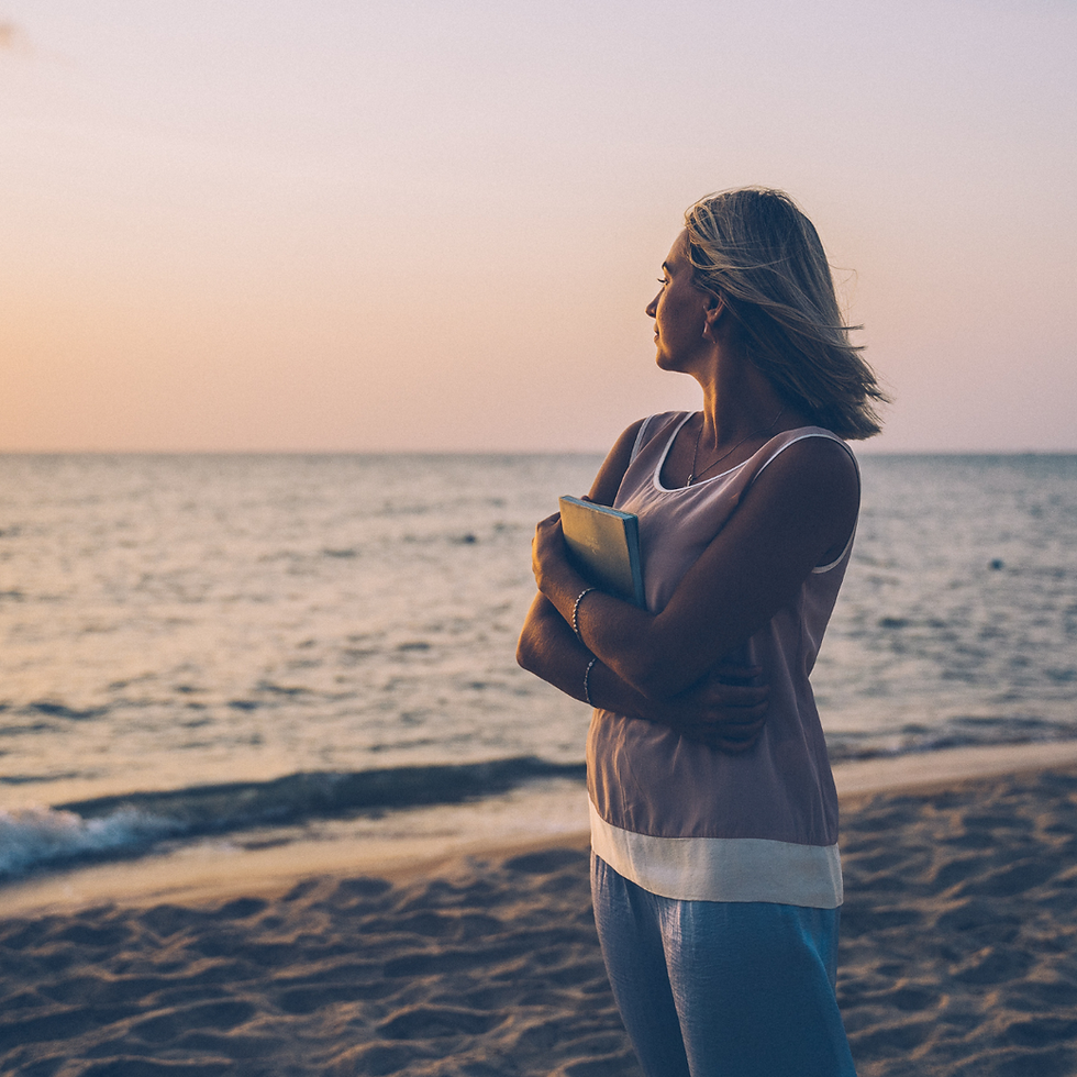 women holding a notebook of stories looking out to sea