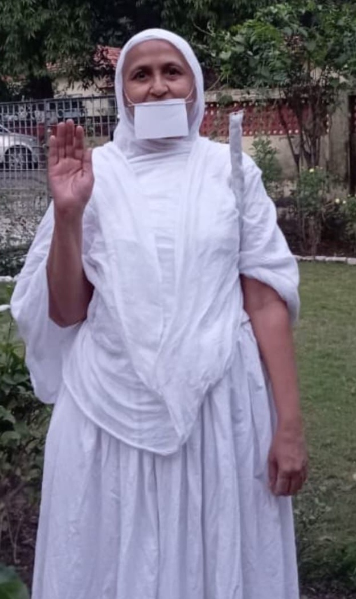 Person in white with mouth covered, hand raised