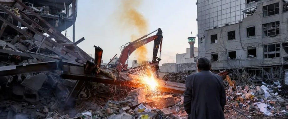 Man watches excavator clearing rubble from Middle East conflict.