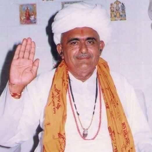Man in white turban and orange scarf, hand raised in blessing