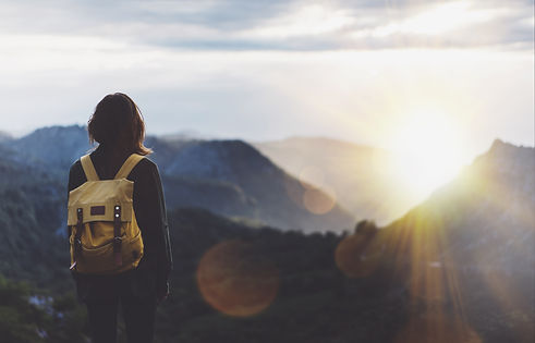 Hipster young girl with backpack enjoying sunset on peak of foggy mountain. Tourist travel