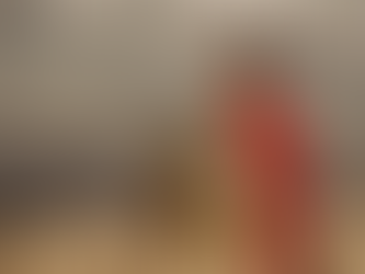 A man in a red cape stands in a field holding a spear and shield under a cloudy sky, evoking a sense of readiness and confidence.