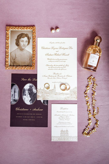A refined wedding flat lay featuring the invitations and wedding programs alongside the bride’s perfume, necklace, rings, and earrings, styled on a soft pink background for an elegant and cohesive detail composition