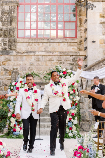A joyful editorial-style photograph of the newlyweds walking down the aisle together after being married, celebrating with their guests in a moment full of emotion and happiness