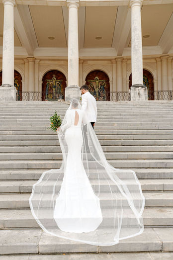 Bride walking up the steps of the Sanctuary of Fátima in Portugal, wearing a minimalist wedding dress with a long cathedral veil