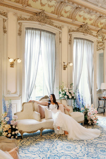 A regal portrait of the bride seated elegantly on a couch inside a palace