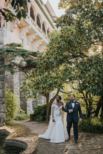 Rhea and Eli walking side by side through the gardens of Casa dos Penedos in Sintra, Portugal, surrounded by greenery and historic stone pathways during their destination wedding.