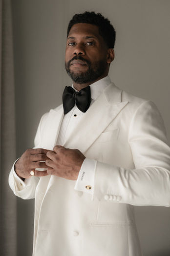 Groom wearing a white tuxedo adjusting his jacket during his wedding preparations at Forte da Cruz in Cascais, Portugal.