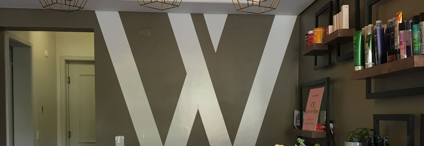 Balcão da recepção do salão com revestimento em padrão chevron, logo estilizado na parede e luminárias pendentes industriais.