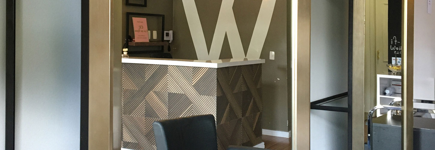 Vista da área de atendimento e poltrona preta, refletida em um espelho, mostrando o balcão da recepção ao fundo.