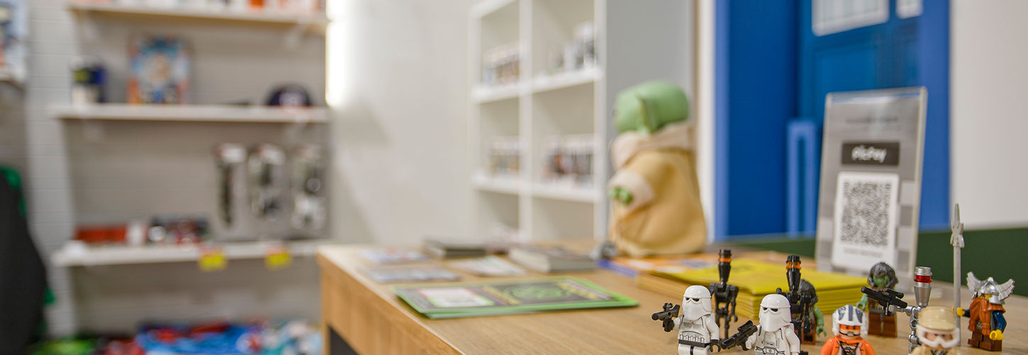 Close-up sobre o balcão de madeira mostrando minifiguras de Lego Star Wars, reforçando a variedade de itens colecionáveis da loja.