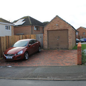 Detached brick garage and block-paved driveway with a red car parked in front