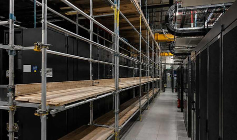Metal scaffolding with wooden planks lining a data center aisle flanked by server racks